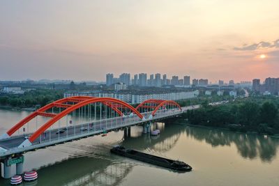Bridge over river by buildings in city against sky during sunset