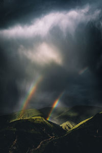 Scenic view of rainbow over mountains against cloudy sky