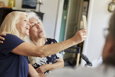 Happy senior friends taking selfie on mobile phone while vlogging at home