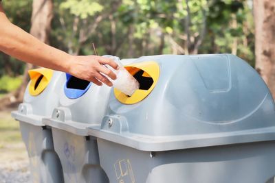 Cropped hand of person holding disposable cup by garbage bin