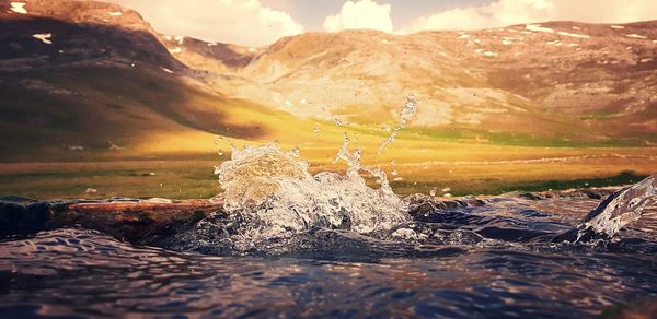 Water splashing on rocks against sky