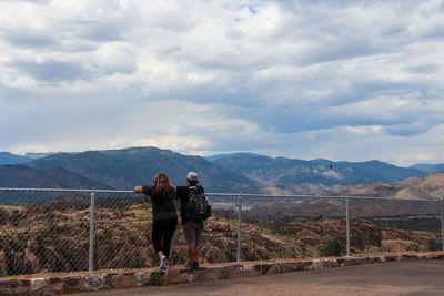 Rear view of friends leaning on railing against mountains