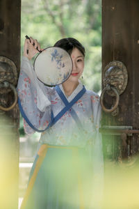 Portrait of woman in kimono holding hand fan at entrance