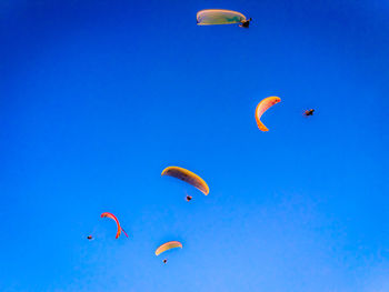 Low angle view of people paragliding against blue sky