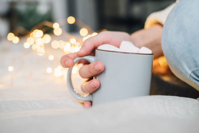 Cropped hand of woman holding marshmallows in mug