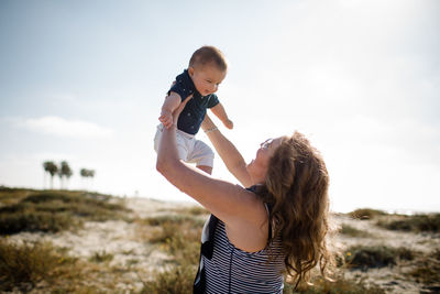 Grandmother holding grandson high while standing on beach