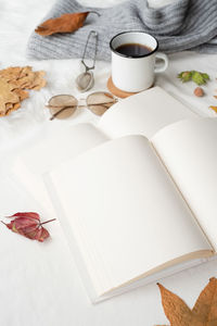 White blank book with autumn leaves and cup of hot tea on old table , mockup design