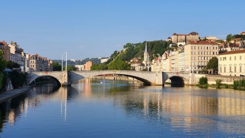 Bridge over river by buildings against clear sky