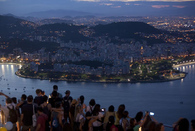 People on illuminated city by sea against sky at night