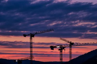 Low angle view of silhouette cranes against sky at sunset