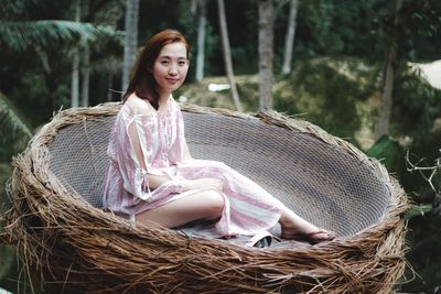 Portrait of smiling woman sitting in basket at forest