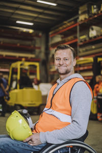 Portrait of carpenter with hardhat sitting on wheelchair in warehouse