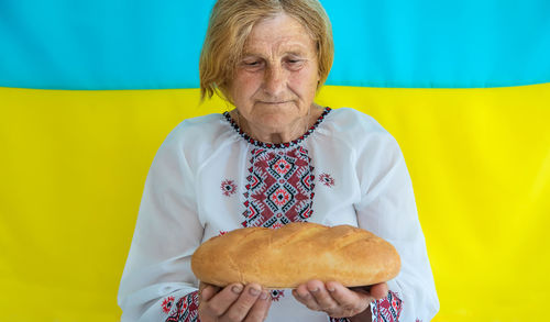 Senior woman holding bread against against ukrainian flag