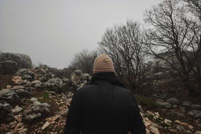 Rear view of man walking on bare trees against clear sky