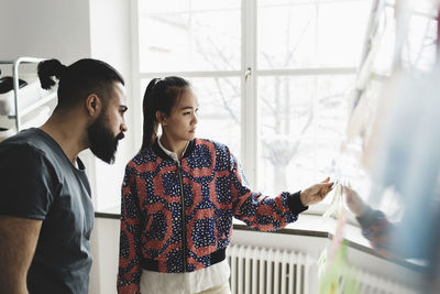 Businesswoman showing male colleague adhesive note on whiteboard in office