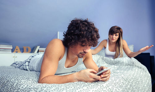 Girlfriend looking at boyfriend using mobile phone on bed at home