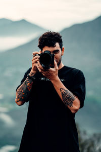 Portrait of young man photographing against sky