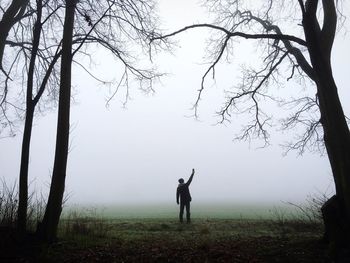 Silhouette man standing on grassy field against sky during foggy weather
