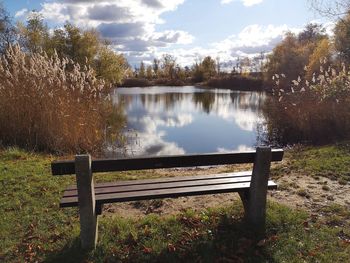 Empty bench by lake against sky