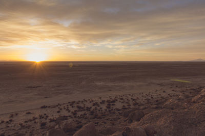 Scenic view of landscape against cloudy sky during sunset