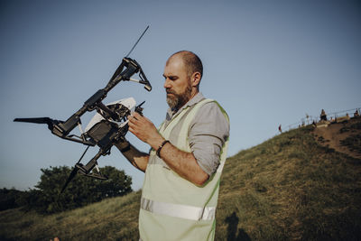 Man holding drone while standing against sky