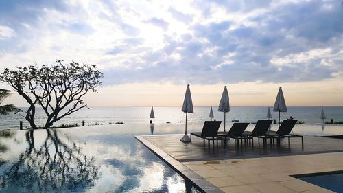 Chairs by swimming pool against sky during sunset