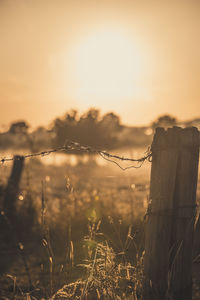 Barbed wire fence on field against sky during sunset