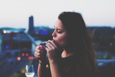 Close-up of woman holding drink in city against sky