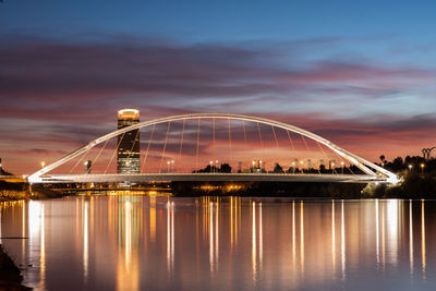 Illuminated bridge over river against sky at night