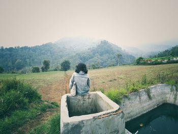 Rear view of man sitting on landscape against sky