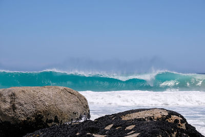 Scenic view of rocks and waves on beach against sky