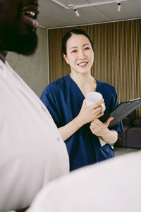 Smiling female nurse holding coffee cup while standing by male doctor at hospital