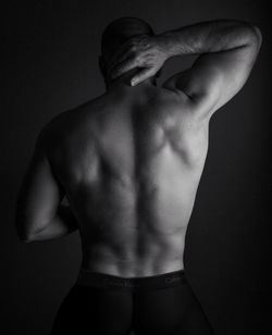 Rear view of shirtless man standing against black background