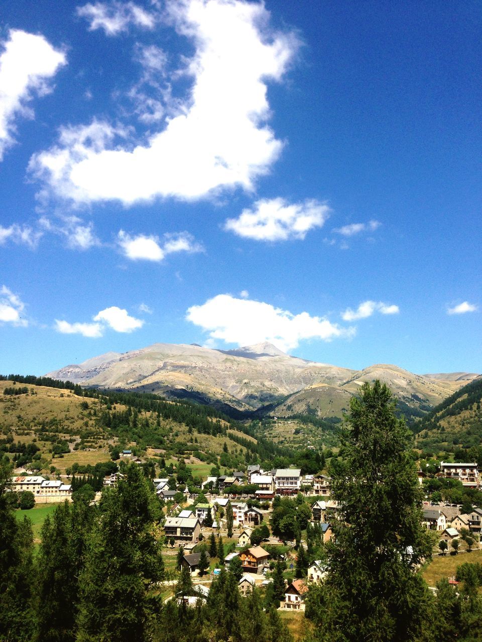 mountain, building exterior, tree, architecture, built structure, sky, mountain range, house, blue, town, high angle view, townscape, landscape, cloud - sky, residential structure, scenics, residential building, residential district, cloud, beauty in nature