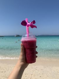 Hand holding pink water on beach against sky