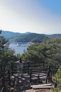 Rear view of man sitting on railing against sky