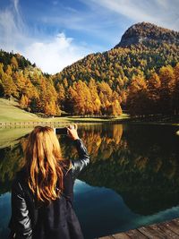 Rear view of woman photographing lake against mountain