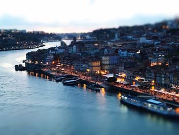 Illuminated buildings by river against sky in city