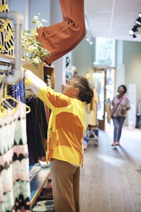 Side view of saleswoman with disability arranging dress on rack while working at store