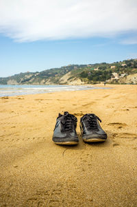 Shoes on sand at beach against sky