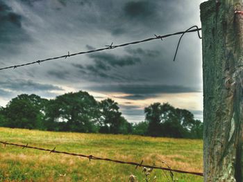 Fence on field against cloudy sky
