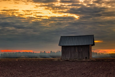 Barn on agricultural field against cloudy sky during sunset