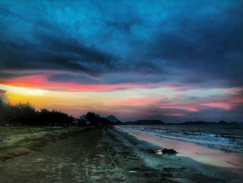 Scenic view of beach against dramatic sky during sunset