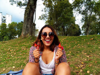 Portrait of smiling woman in sunglasses holding strawberries while sitting on field