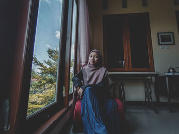 Portrait of young woman standing by window