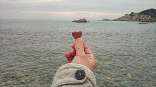 Cropped image man holding heart shape pebble in front of sea
