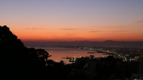 High angle view of illuminated buildings by sea against sky during sunset