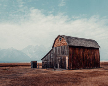 Barn on field by houses against sky