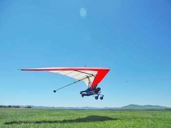 People paragliding over field against clear blue sky