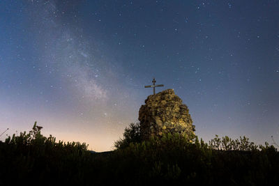 Milky way over the ruins of a castle, with a metallic cross.